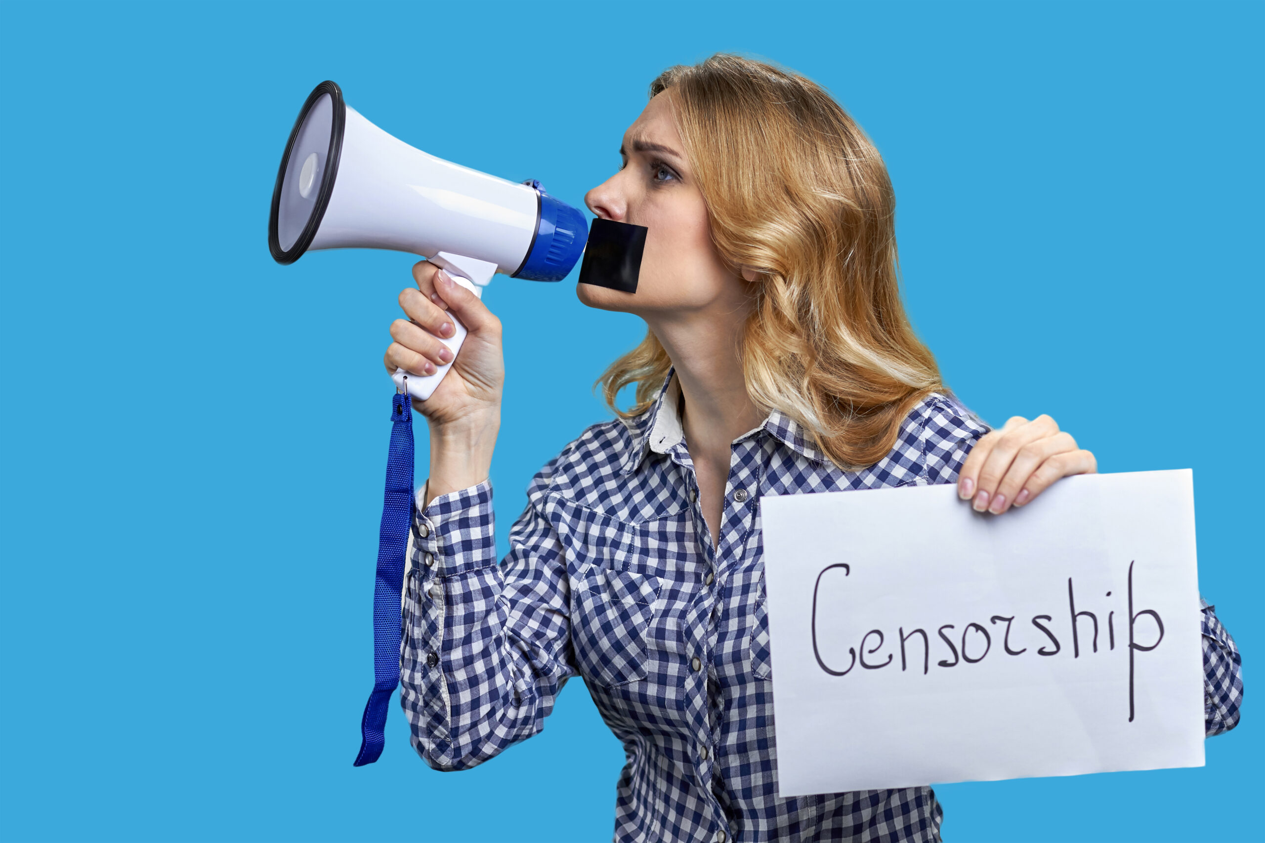 Young blonde woman holding megaphone and banner with censorship inscription. Female protestor with mouth taped on blue background.