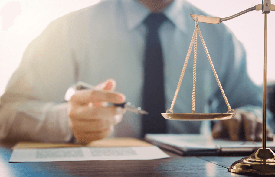 Advogado com caneta sobre a mesa e balança da justiça, fazendo referência à ajuda especializada no TAC no processo administrativo disciplinar .