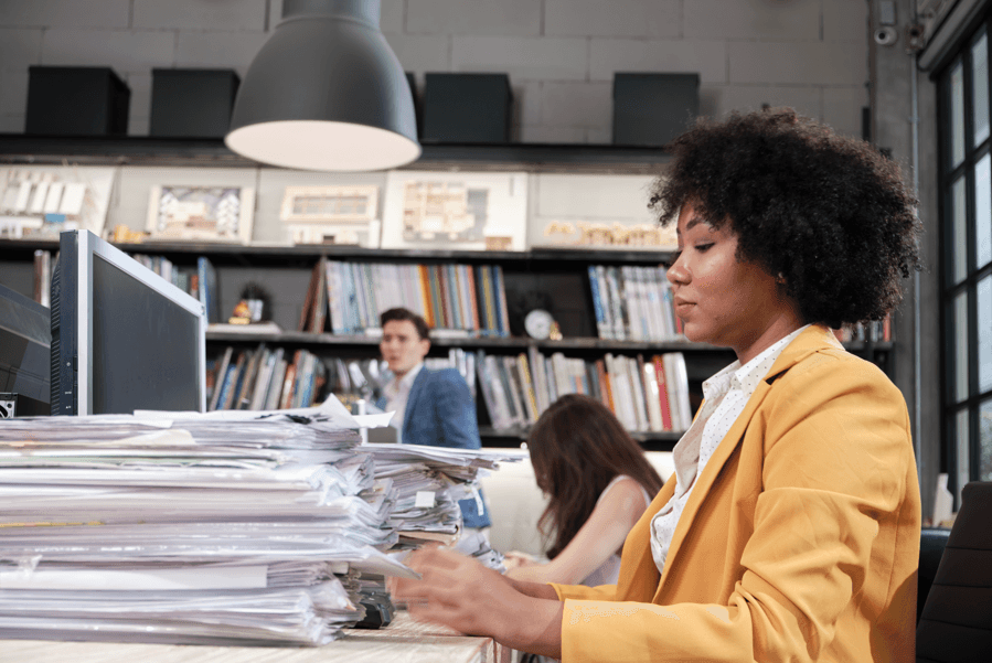 Mulher com pilha de documentos para analisar, fazendo referência aos direitos no Processo Administrativo Disciplinar.