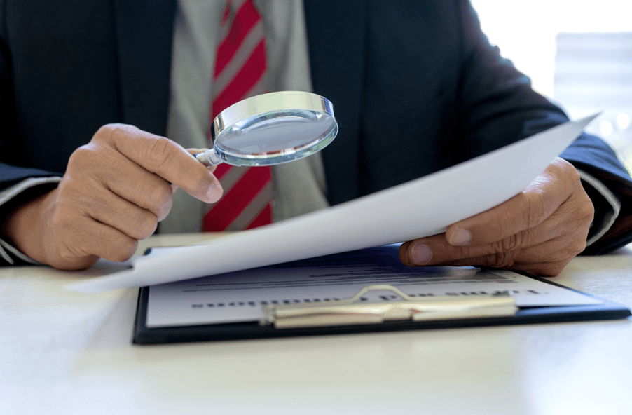 Homem analisando documento com lupa, fazendo referência à estrutura e ao conteúdo do relatório final no processo administrativo disciplinar.