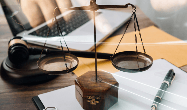 Notebook, martelo, caneta, papel e balança da justiça sobre a mesa, fazendo referência à prática do advogado num PAD por incontinência pública. 