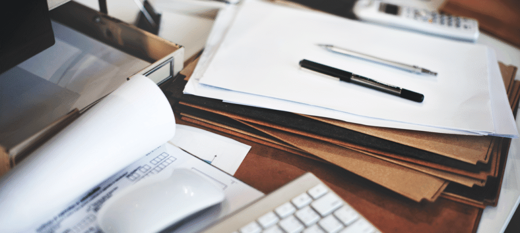 Sindicância no serviço público: pilha de papéis, pastas e canetas sobre a mesa.