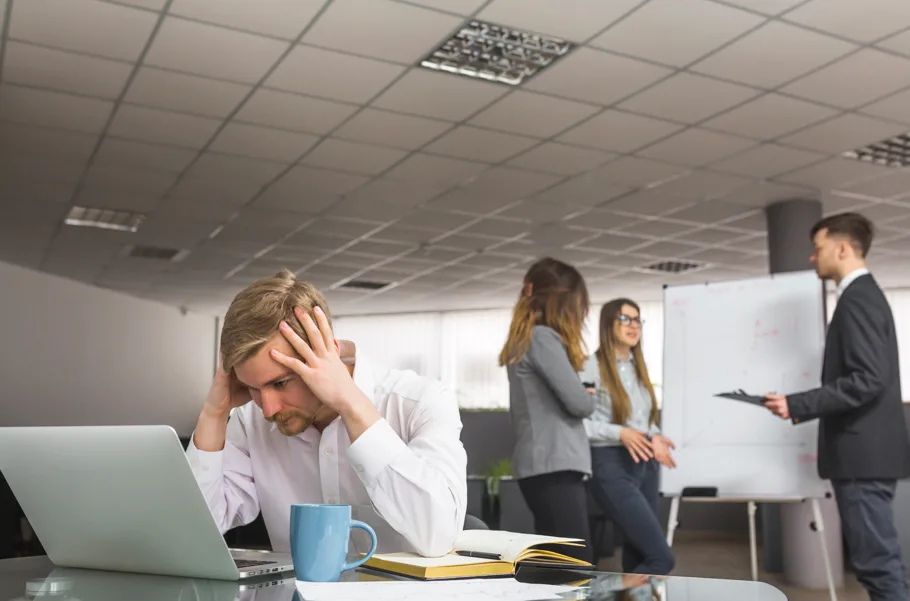 Como provar que a depressão do servidor público foi causada pelo trabalho: homem sofrendo no trabalho e equipe reunida atrás,