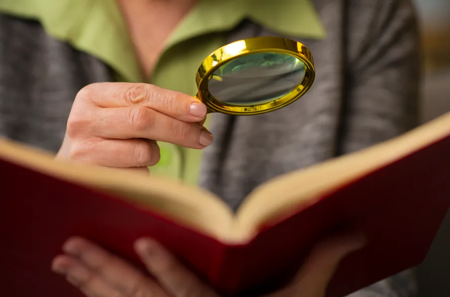 A desproporcionalidade da penalidade no Processo Administrativo Disciplinar: mulher com lupa sobre livro simbolizando análise.